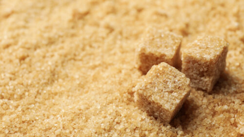 Brown sugar cubes on sugar background, space for text